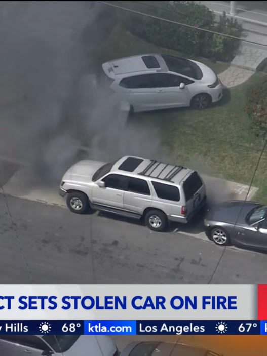 Aerial view of a silver SUV smoking as it sits on a residential street, breaking news banner at bottom reading 'Pursuit Suspect Sets Stolen Car on Fire'.