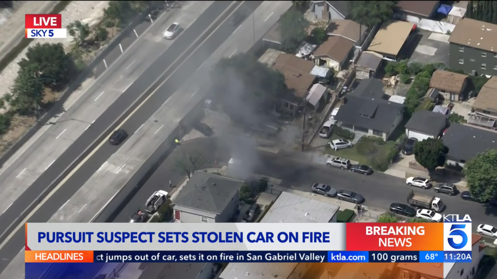 Aerial view of a residential street with smoke rising from a car fire after a pursuit; breaking news banner at the bottom showing KTLA 5 on air.