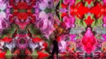 Person silhouetted in front of a large kaleidoscopic mural with pink, red, purple, and green floral patterns on a wall inside an installation.
