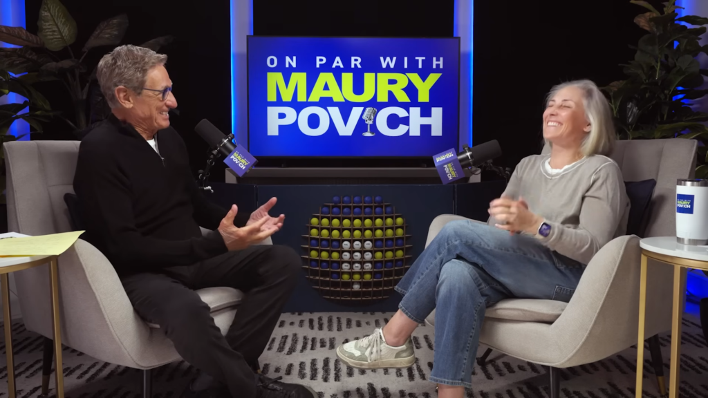 Two people sit in talking chairs on a podcast set, smiling at each other with microphones and a sign reading 'On Par with Maury Povich' behind them.
