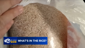 Close-up of a bag of uncooked white rice held in a plastic bag, with a blue ABC7 On Your Side banner reading 'WHAT'S IN THE RICE?'