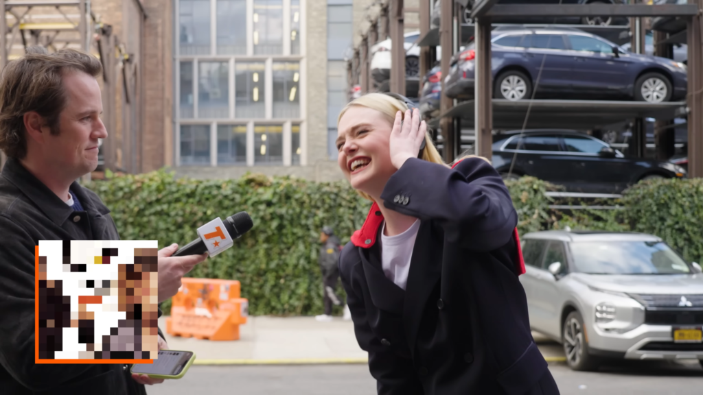 Reporter interviews a laughing woman in a navy blazer outdoors, with parked cars and orange barriers in the background.