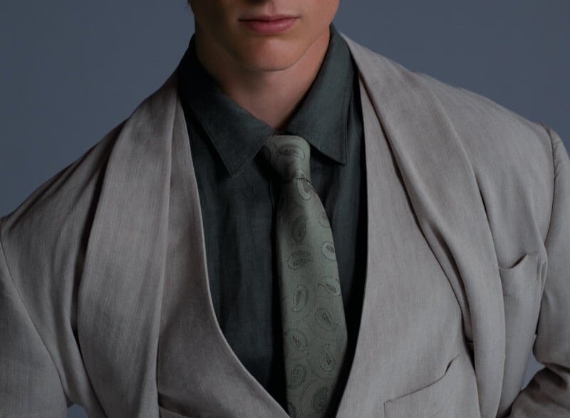Portrait of a young man in a light gray suit, vest, and paisley tie, wearing a cap and tinted glasses.