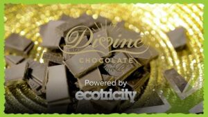 Divine Chocolate logo over a pile of dark chocolate chunks with a gold bokeh background, captioned 'Powered by ecotricity'
