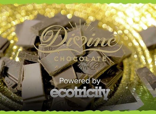 Divine Chocolate logo over a pile of dark chocolate chunks with a gold bokeh background, captioned 'Powered by ecotricity'