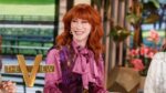 Smiling red-haired woman in a pink blouse and purple vest sits at a talk-show set with the 'THE VIEW' logo visible in the foreground.