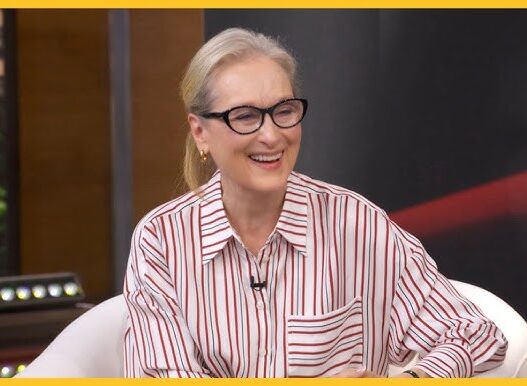 Smiling blonde woman with black glasses in a red-striped shirt on a TV morning-show set (GMA).