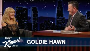 Goldie Hawn on a late-night set with Jimmy Kimmel, both smiling during an interview, backdrop of a city skyline and show banner reading 'Goldie Hawn' and 'Jimmy Kimmel Live'.