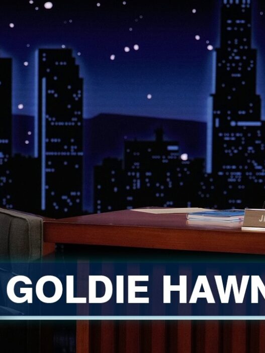 Goldie Hawn on a late-night set with Jimmy Kimmel, both smiling during an interview, backdrop of a city skyline and show banner reading 'Goldie Hawn' and 'Jimmy Kimmel Live'.