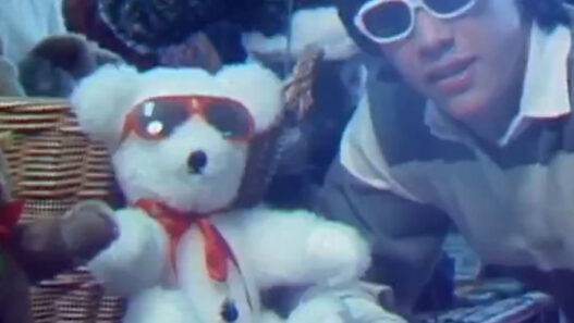 Young Keanu Reeves interviewing teddy‑bear collectors as a CBC reporter in a vintage TV segment.