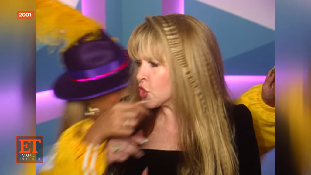Blonde woman on a colorful TV set with a person in a yellow outfit nearby; ET Vault Unlocked logo visible in the corner.