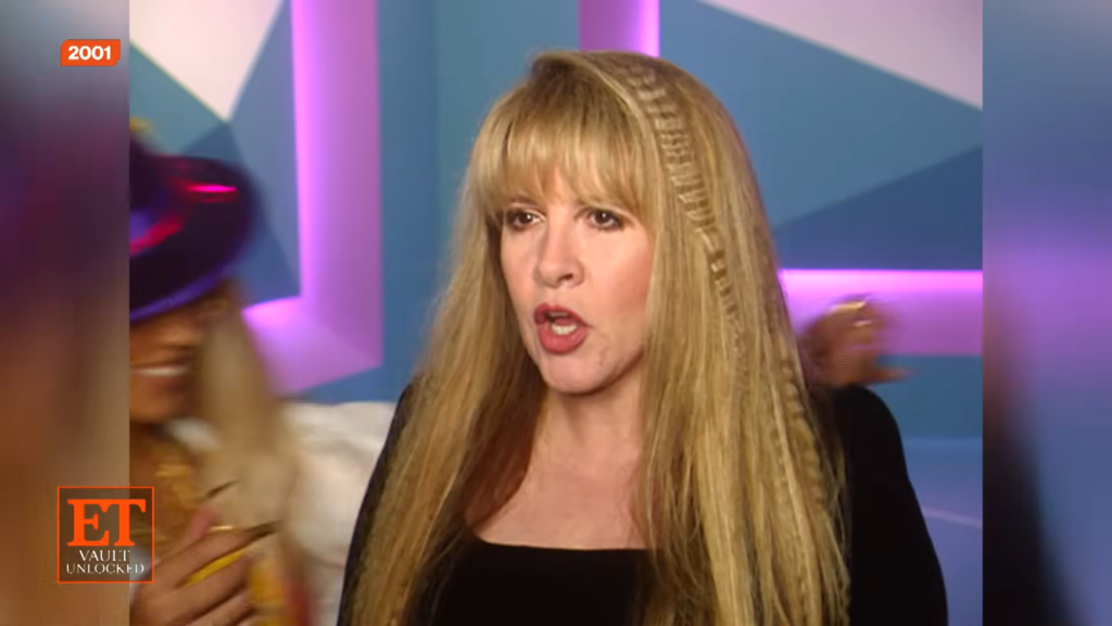 Blonde woman speaking on a TV set with a colorful geometric backdrop and ET logo in the corner.