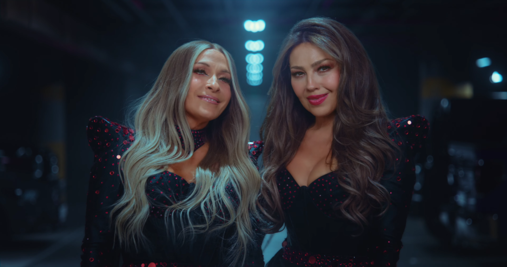 Two women in matching black sequined outfits smile at the camera backstage.