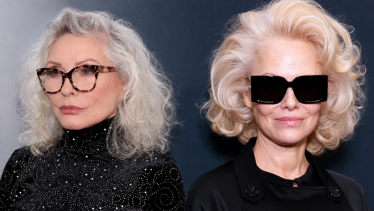 Side-by-side cropped headshot composite of Debbie Harry and Pamela Anderson in sleek black fashion looks, styled with silver and platinum blonde hair for an entertainment story header.