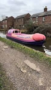 A sleek, phallic‑shaped narrowboat gliding smoothly along a quiet canal.