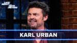Smiling male guest on a late-night talk show, with 'KARL URBAN' text overlay and blue neon horizontal lines across the frame.