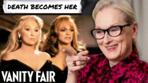 Collage: two women in elegant dresses on the left, older woman with glasses on the right smiling and pointing; 'Death Becomes Her' banner top, 'Vanity Fair' text bottom left.