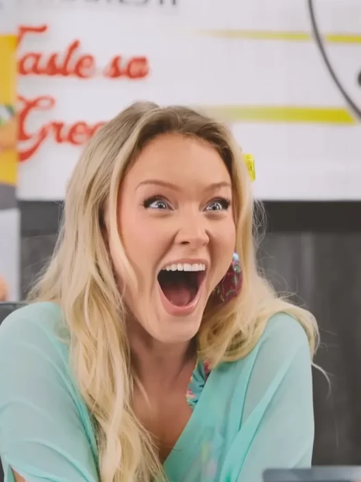 Blonde woman with a surprised, open-mouthed expression in a restaurant or food stall setting