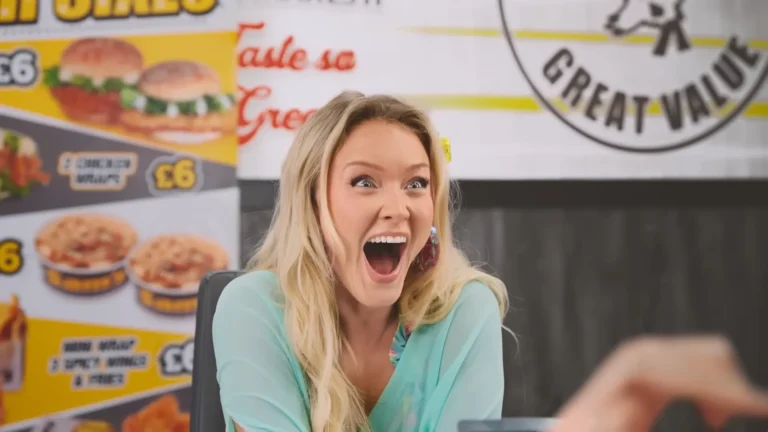 Blonde woman with a surprised, open-mouthed expression in a restaurant or food stall setting