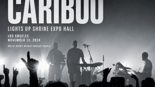 Caribou performs live at Shrine Expo Hall in Los Angeles on November 13, 2024, silhouetted against dramatic backlighting as the crowd raises their hands.
