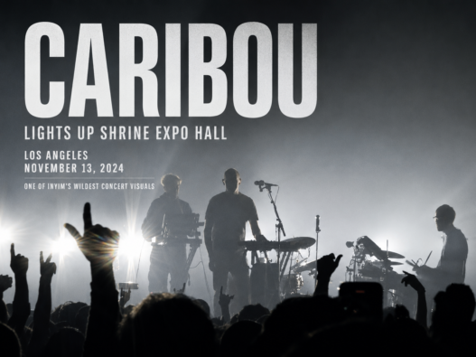 Caribou performs live at Shrine Expo Hall in Los Angeles on November 13, 2024, silhouetted against dramatic backlighting as the crowd raises their hands.
