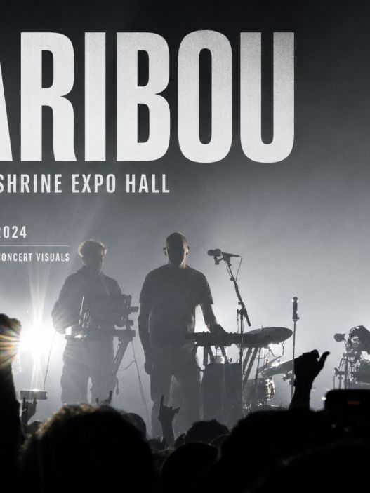 Caribou performs live at Shrine Expo Hall in Los Angeles on November 13, 2024, silhouetted against dramatic backlighting as the crowd raises their hands.