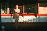 Frankie June standing in warm sunlight outside a red-and-white storefront holding an ice cream cone