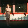 Frankie June standing in warm sunlight outside a red-and-white storefront holding an ice cream cone