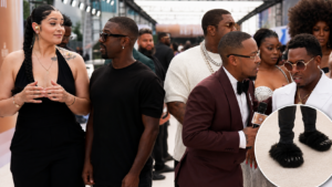 Ray J reacts awkwardly on the BET Awards 2026 red carpet beside a sign language interpreter, with a circular close-up of his black furry slipper-style footwear.