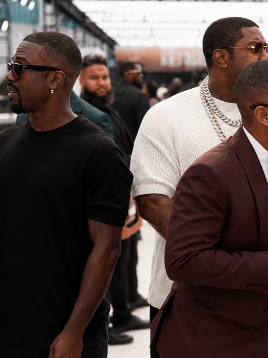 Ray J reacts awkwardly on the BET Awards 2026 red carpet beside a sign language interpreter, with a circular close-up of his black furry slipper-style footwear.