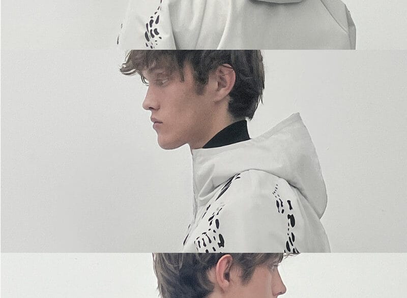 Two close portrait views of a model wearing a black HELIOT EMIL SS27 jacket with an oversized high collar and silver hardware