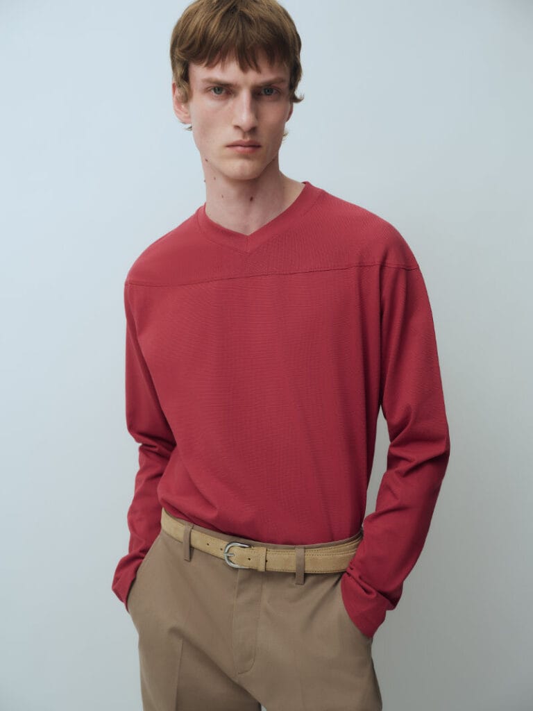 Model wears a red long-sleeved knit top with camel trousers in ARKET’s Fall Winter 2026 collection