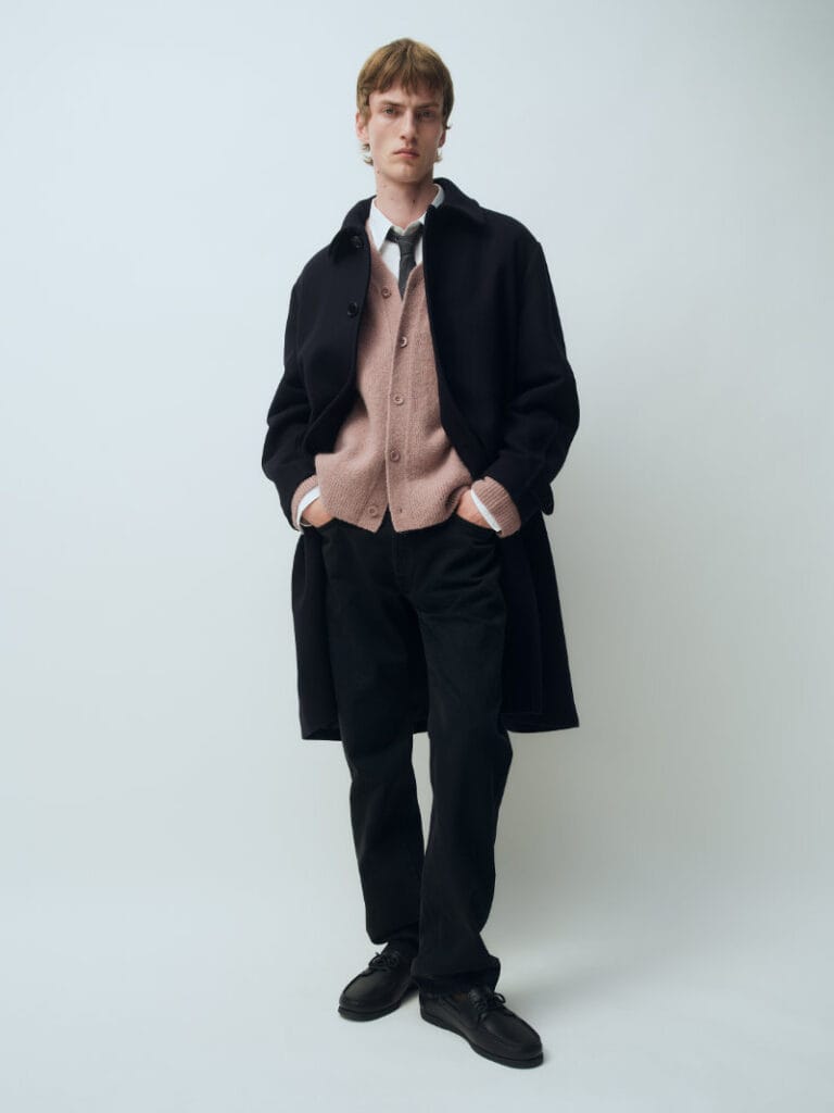 Model layers a black coat over a dusty pink cardigan, white shirt and tie for ARKET Fall Winter 2026