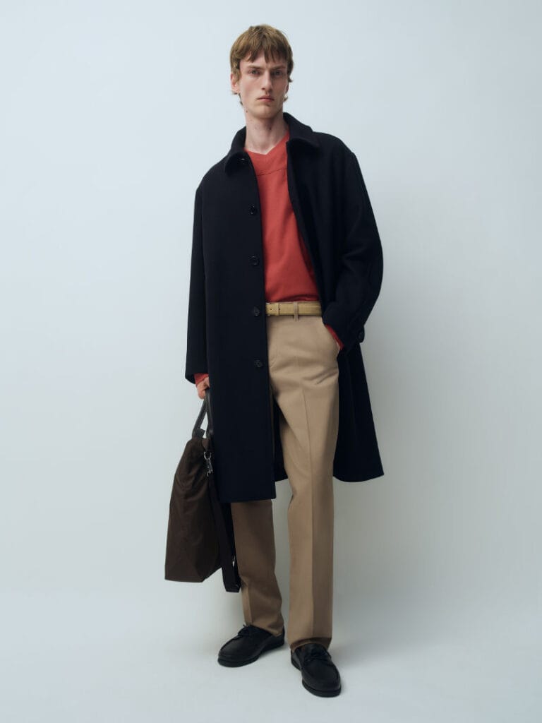 Model wears a navy overcoat with a red top and camel trousers from ARKET’s Fall Winter 2026 collection