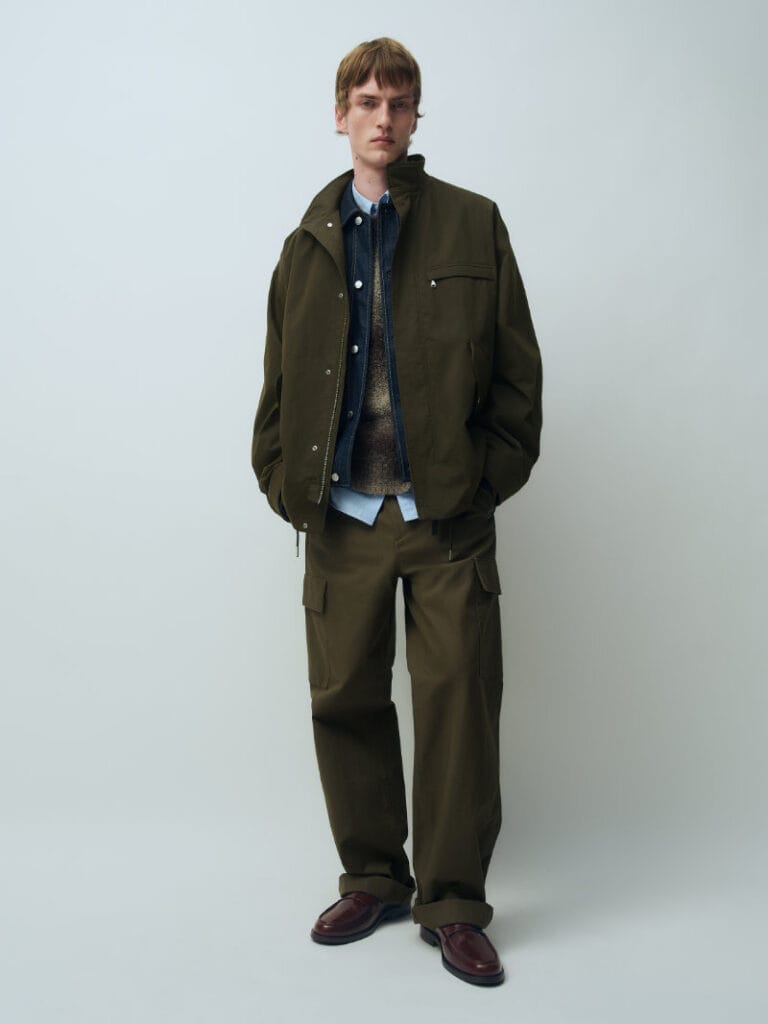 Model wears layered olive utility outerwear and cargo trousers from ARKET’s Fall Winter 2026 collection