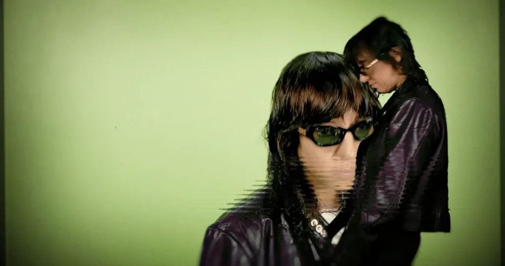 Distorted duplicate portraits of Chloé Caillet in a purple leather jacket and sunglasses against green