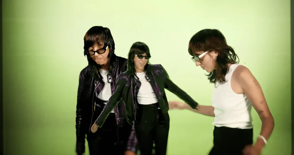 Three overlapping versions of Chloé Caillet dancing in sunglasses against a green screen in the Bad Bara video