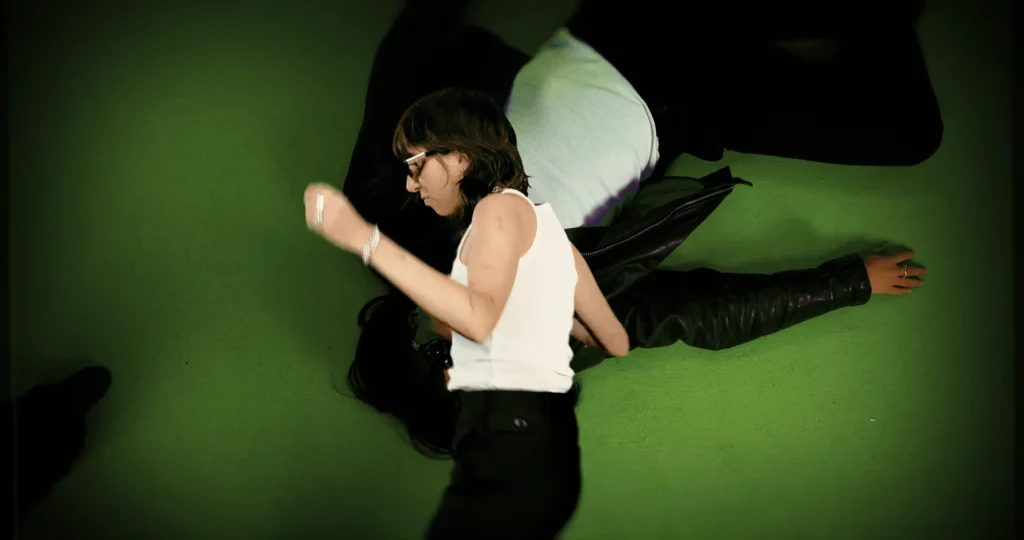 Chloé Caillet dancing over an enlarged duplicate of herself lying across a green background
