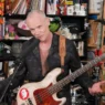 Flea speaking at the NPR Tiny Desk with his bass strapped across his chest during the Honora Band performance