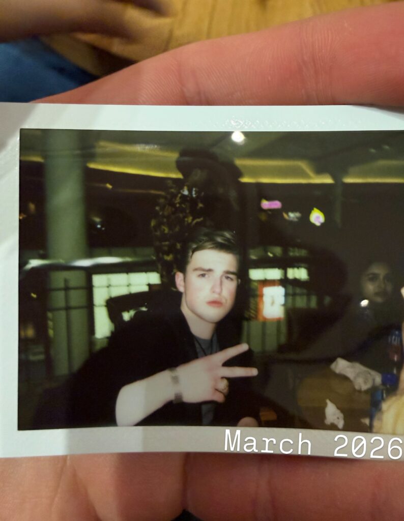 Instant photo of Iain Armitage holding up a peace sign in March 2026
