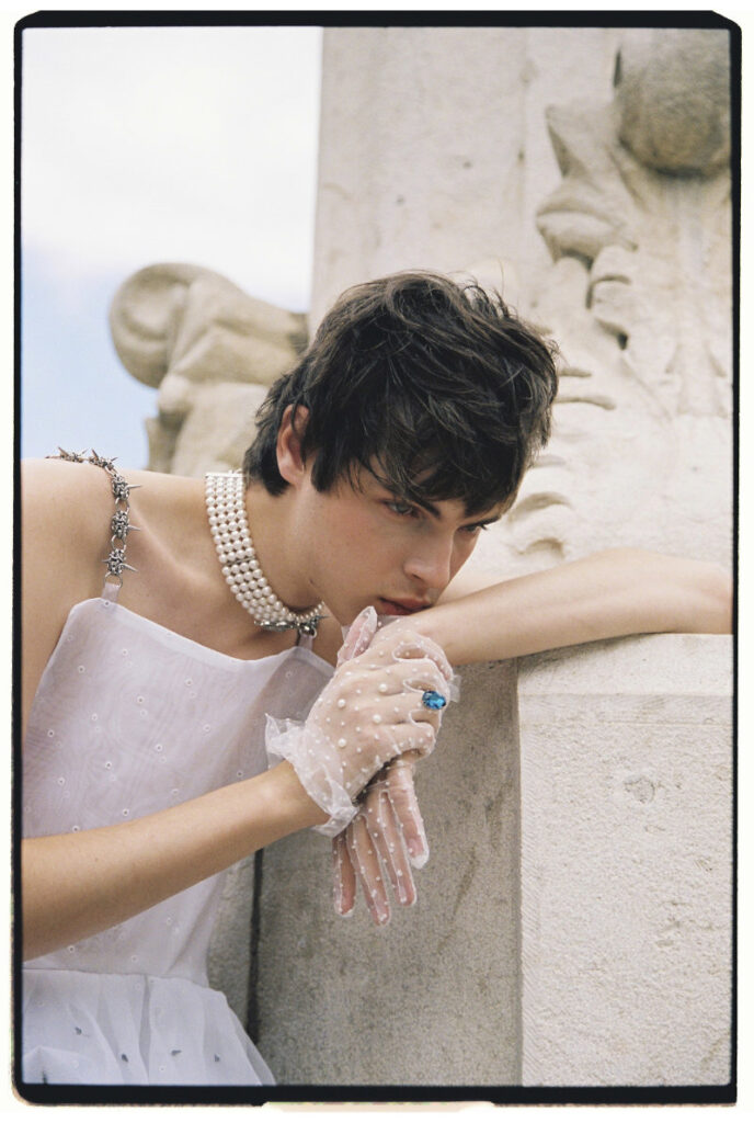 Close portrait of Ruslan in a white top, layered pearl choker and sheer embellished gloves