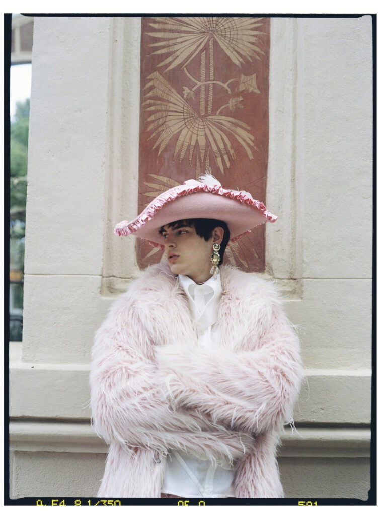 Close portrait of Ruslan in a pink faux-fur coat, white shirt and ruffled pink hat