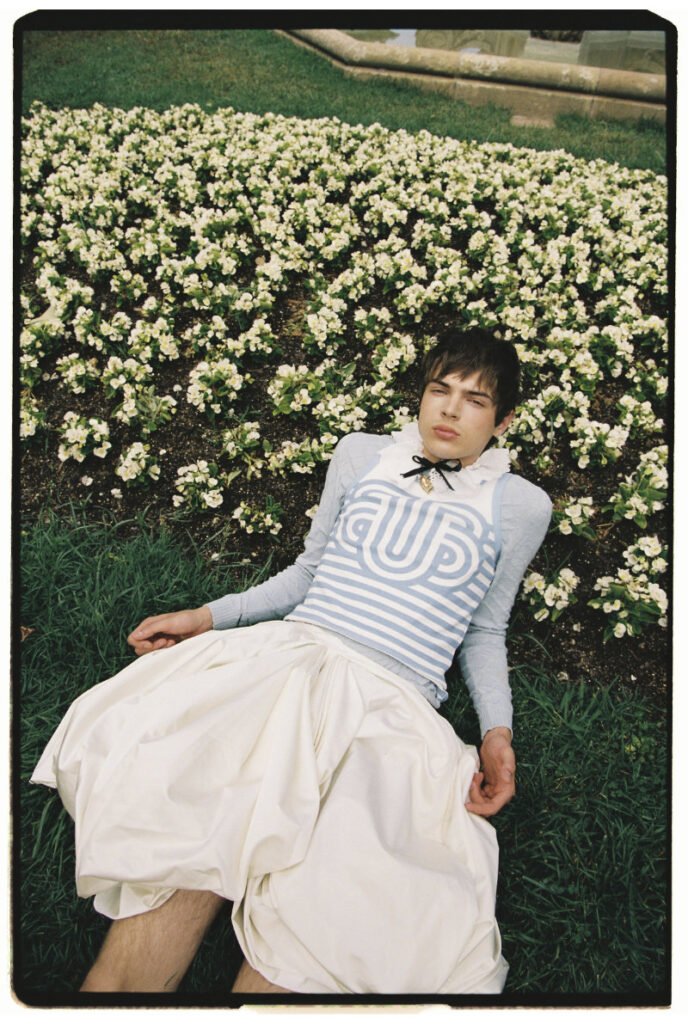 Ruslan reclining beside white blossoms in a striped blue top and voluminous white skirt
