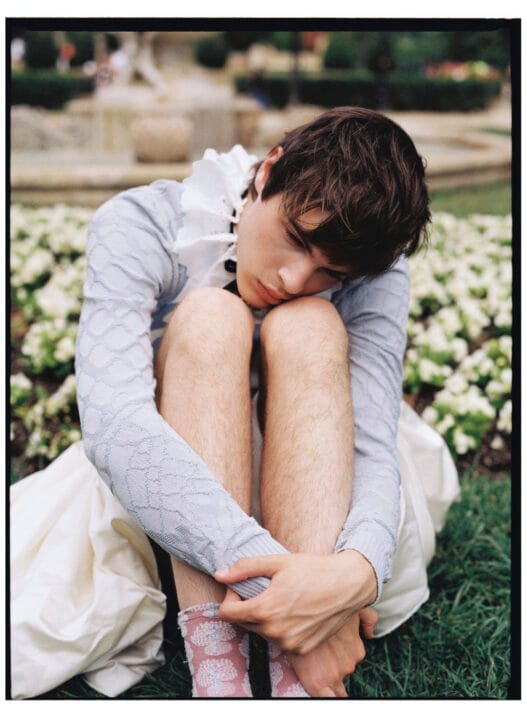 Ruslan seated in a pale blue knit top and voluminous white skirt for The It Boy of Versailles editorial