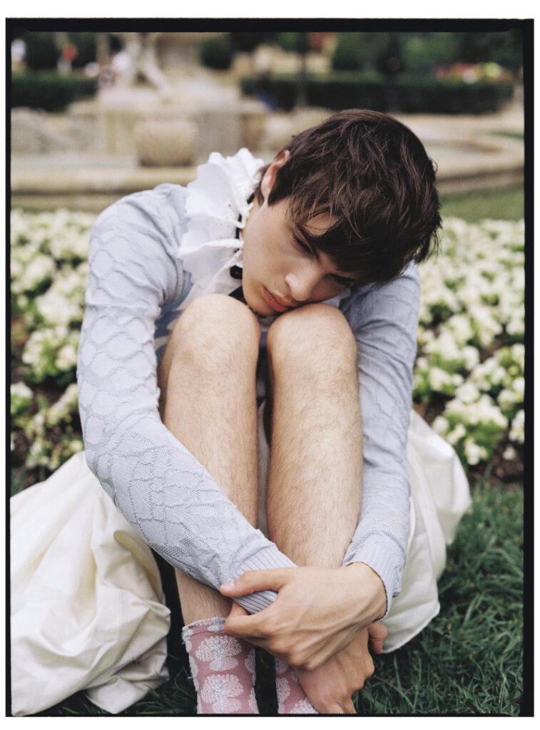 Ruslan seated in a pale blue knit top and voluminous white skirt for The It Boy of Versailles editorial