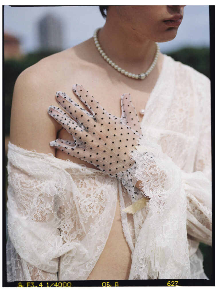 Close-up of Ruslan in white lace, a pearl necklace and sheer polka-dot gloves