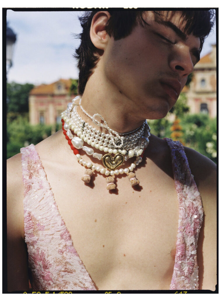 Close portrait of Ruslan wearing layered pearl necklaces and a pink embellished top