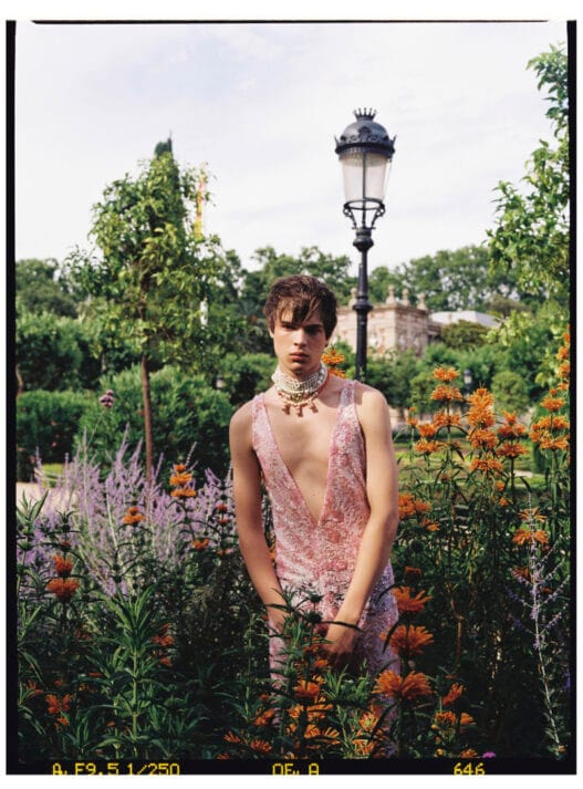 Ruslan wearing a deep pink embellished jumpsuit and layered pearl necklaces in a formal garden