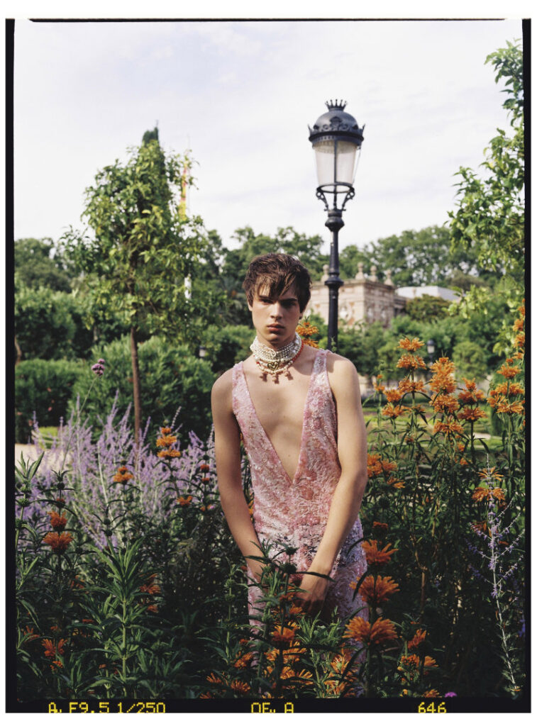 Ruslan wearing a deep pink embellished jumpsuit and layered pearl necklaces in a formal garden