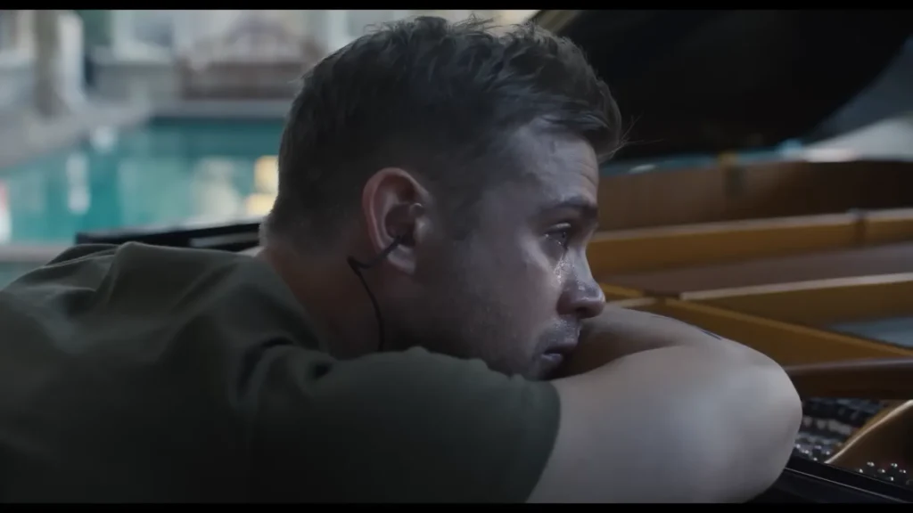 Man wearing an earpiece resting beside an open piano in Tuner